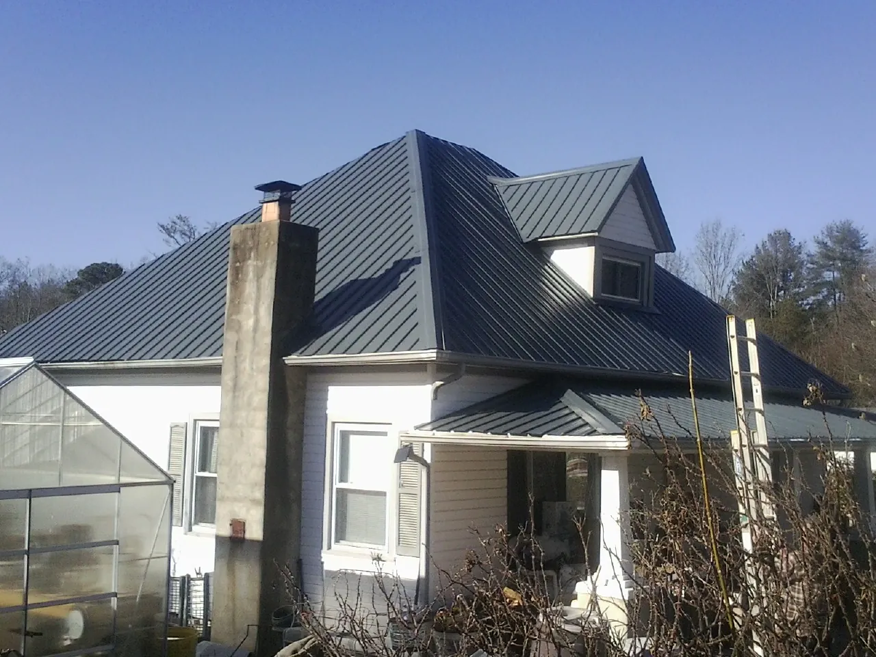 Dark blue standing seam metal roof on a white farmhouse with dormer — Slate & Tile Roof Repair by Roofing Brothers in Clarkston