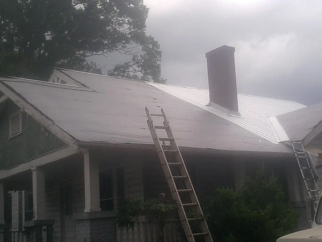 Ladders against a metal roof on an older home with a brick chimney in Clarkston